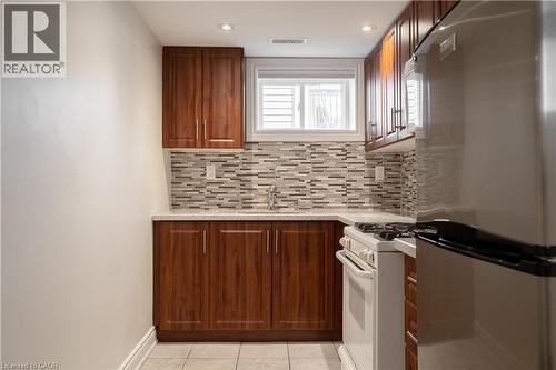 Kitchen featuring wood-finish cabinetry, tile backsplash, stone-finish countertops, stainless steel refrigerator, and a white range - 50 Norway Avenue, Hamilton, ON 