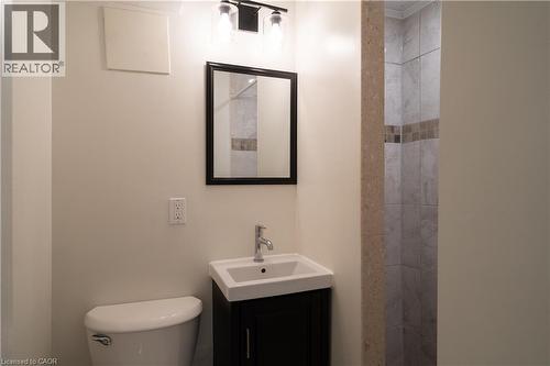 Bathroom featuring a contemporary vanity with an integrated sink, polished chrome faucet, framed mirror, and a tiled shower with decorative accent banding - 50 Norway Avenue, Hamilton, ON 