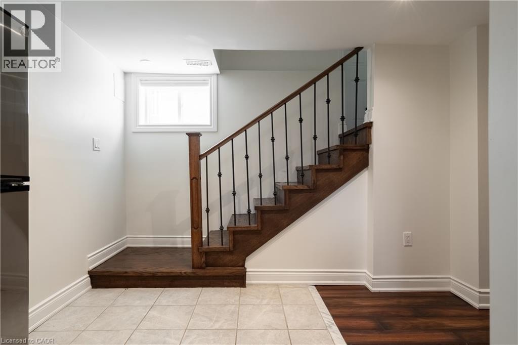 Hardwood staircase with wrought iron balusters, white trim, and wood-finish flooring - 50 Norway Avenue, Hamilton, ON