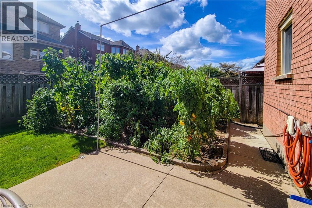 Private backyard with concrete patio, garden bed with mature plants, and wood privacy fencing - 276 Greencedar Drive, Hamilton, ON