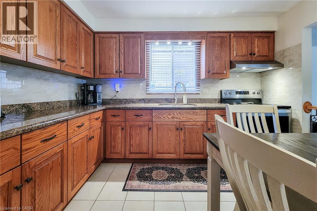 Kitchen featuring wood cabinetry, solid surface countertops, tile backsplash, stainless steel appliances, and tile flooring - 276 Greencedar Drive, Hamilton, ON