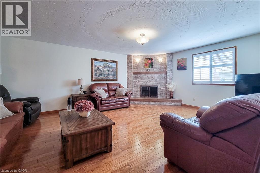 Wood-finish flooring throughout, a white brick fireplace with a wood mantle, white plantation shutters, and recessed ceiling lighting - 276 Greencedar Drive, Hamilton, ON