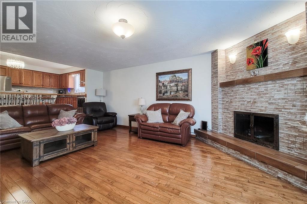 Hardwood flooring throughout, stone fireplace with a wood mantel, overhead lighting, and an open-concept layout - 276 Greencedar Drive, Hamilton, ON