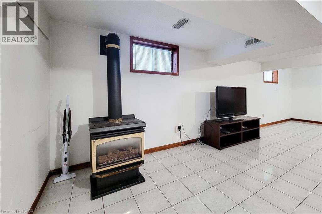 Freestanding fireplace with a black flue, white tile flooring, and wood-trimmed windows - 276 Greencedar Drive, Hamilton, ON