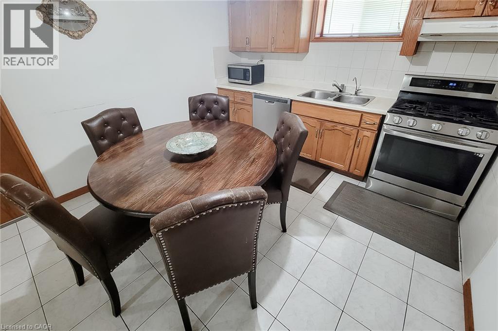 Kitchen area featuring white tile flooring, stainless steel gas range, stainless steel dishwasher, double basin sink, and light wood cabinetry - 276 Greencedar Drive, Hamilton, ON