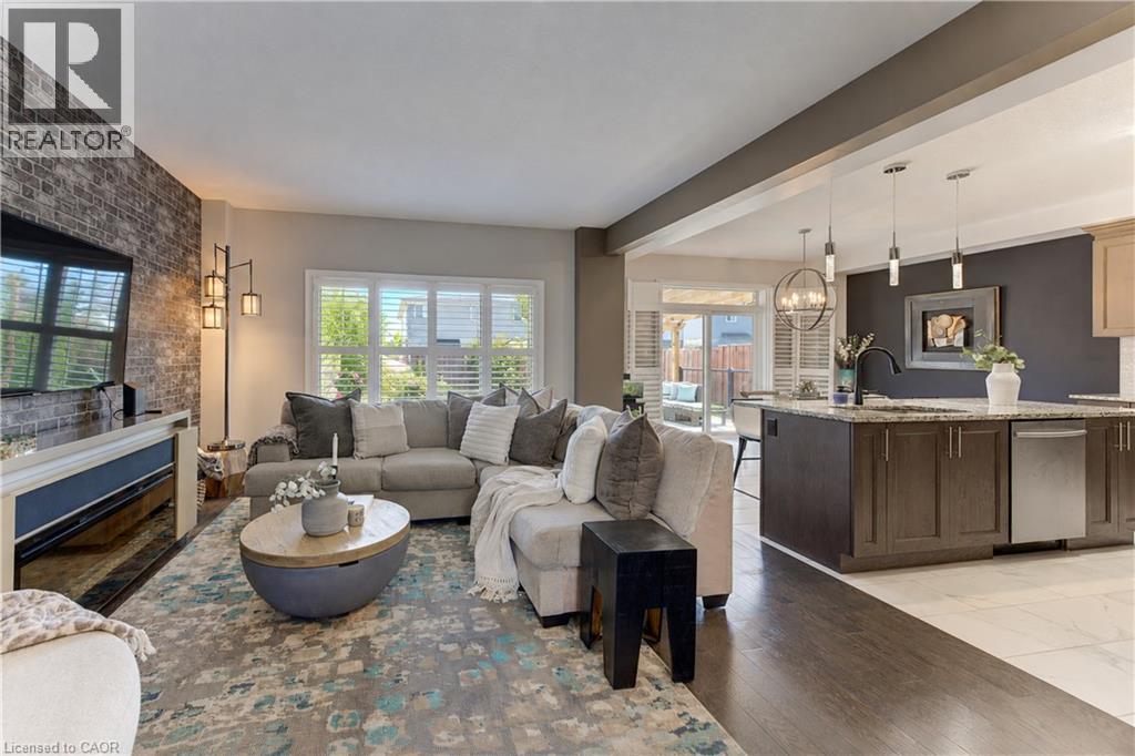 Living area featuring a brick accent wall, wood-finish flooring, and white plantation shutters - 428 Freure Drive, Cambridge, ON