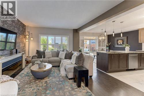 Living area featuring a brick accent wall, wood-finish flooring, and white plantation shutters - 428 Freure Drive, Cambridge, ON 