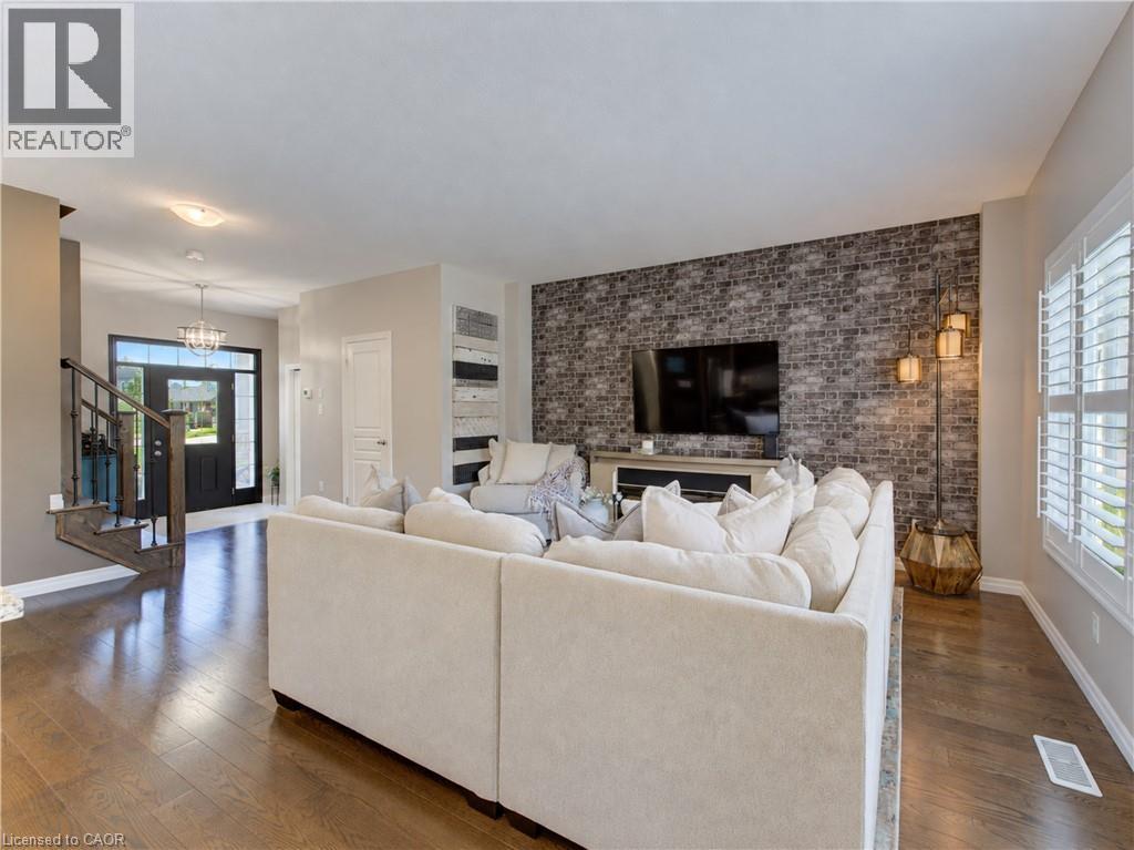 Hardwood flooring throughout the living area, brick-finish accent wall, window with plantation shutters, staircase with wrought iron balusters, and a front entry door with sidelights - 428 Freure Drive, Cambridge, ON