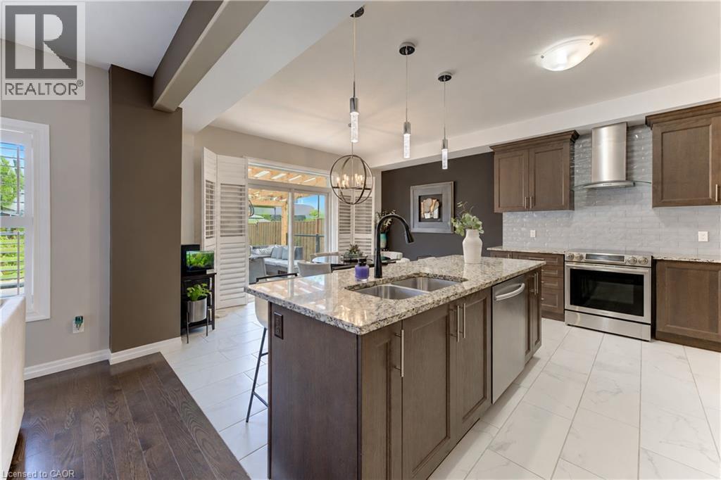Kitchen featuring a central island with dual sinks, stone countertop, and pendant lighting - 428 Freure Drive, Cambridge, ON