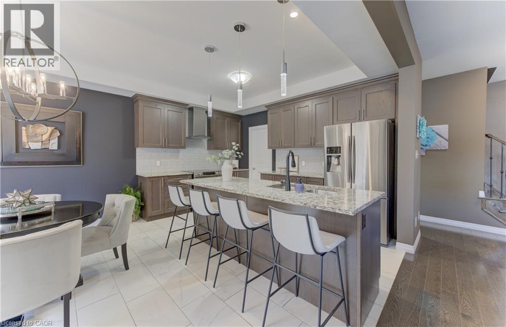 Kitchen featuring wood-finish cabinetry, stainless steel appliances, a large center island with a stone countertop, and a tile backsplash - 428 Freure Drive, Cambridge, ON