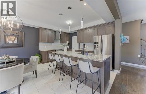 Kitchen featuring wood-finish cabinetry, stainless steel appliances, a large center island with a stone countertop, and a tile backsplash - 428 Freure Drive, Cambridge, ON 