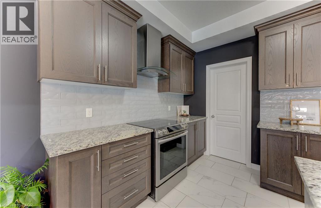 Kitchen featuring wood-finish cabinetry, light-toned countertops, a subway tile backsplash, stainless steel appliances, and large format floor tiles - 428 Freure Drive, Cambridge, ON