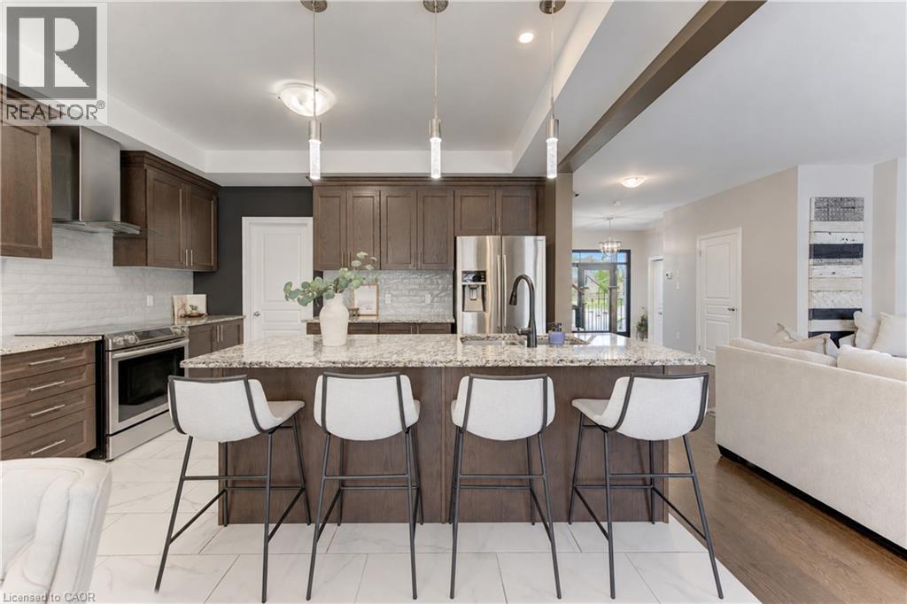 Kitchen featuring wood-finish cabinetry, stainless steel appliances, granite island with seating, and subway tile backsplash - 428 Freure Drive, Cambridge, ON