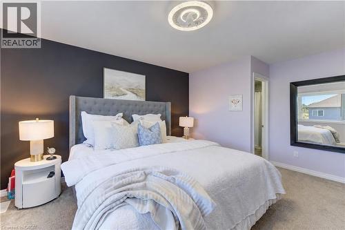 Tufted upholstered headboard, dual bedside lamps, carpet flooring, ceiling-mounted light fixture, and a framed wall mirror - 428 Freure Drive, Cambridge, ON 