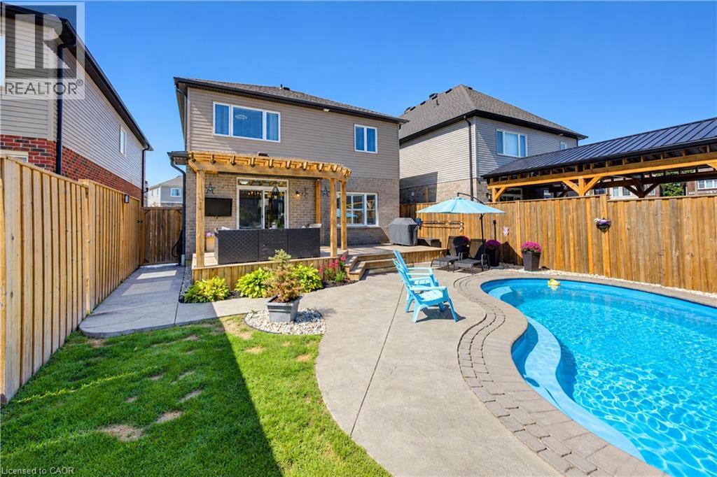 Landscaped backyard featuring an in-ground swimming pool, concrete patio, and a wood-frame pergola over a deck - 428 Freure Drive, Cambridge, ON