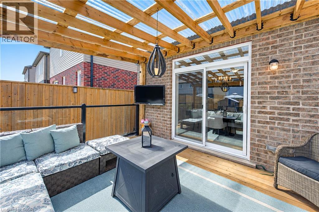 Covered patio with wood decking, brick exterior, wood pergola with clear roofing, and a sliding glass door - 428 Freure Drive, Cambridge, ON