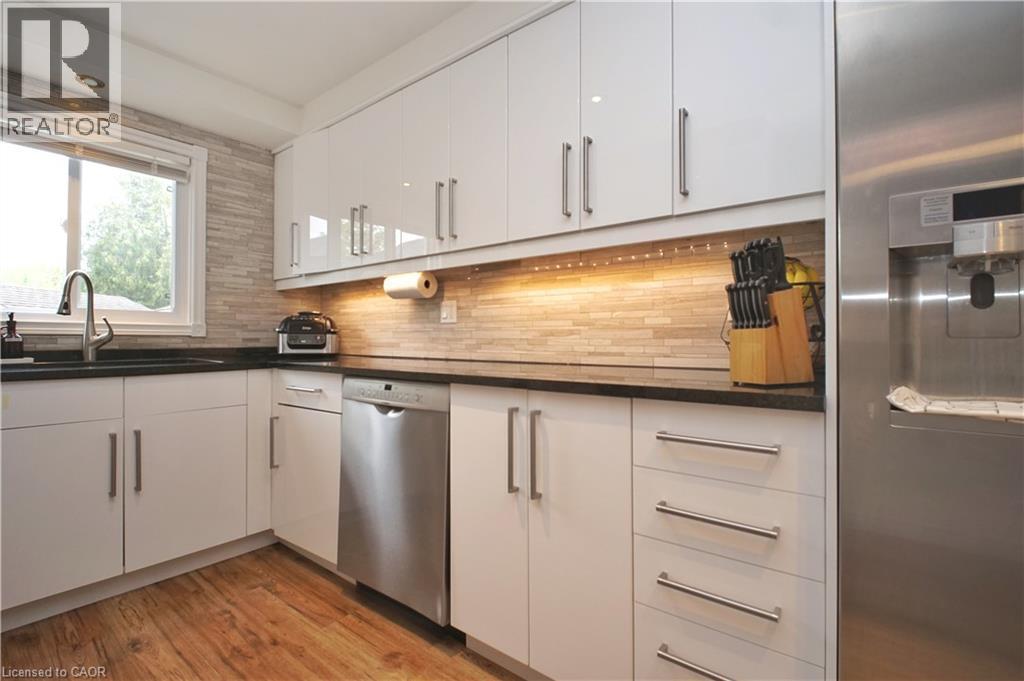 White cabinetry with brushed nickel hardware, dark countertops, wood-finish flooring, and a tiled backsplash - 380 Grangewood Drive, Waterloo, ON