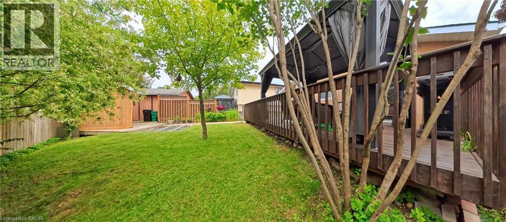 Expansive backyard featuring a manicured lawn, established trees, and a wooden privacy fence - 380 Grangewood Drive, Waterloo, ON