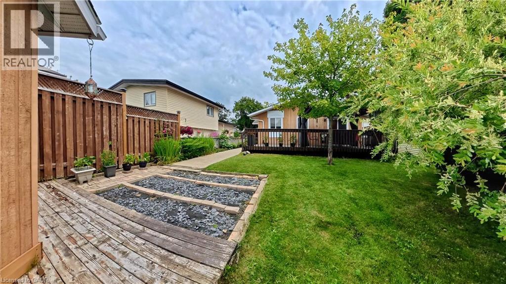 Expansive backyard featuring a manicured lawn, a full-width wood deck, and raised garden beds - 380 Grangewood Drive, Waterloo, ON