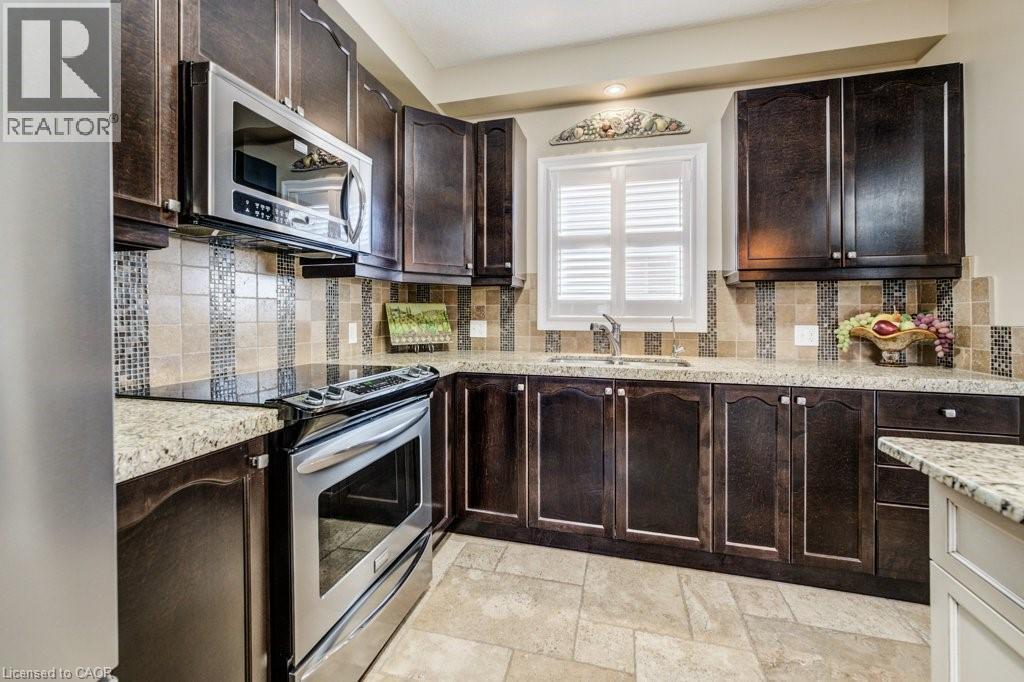 Kitchen featuring dark wood cabinetry, light granite countertops, a stainless steel range, and an over-range microwave - 300 Watervale Crescent, Kitchener, ON