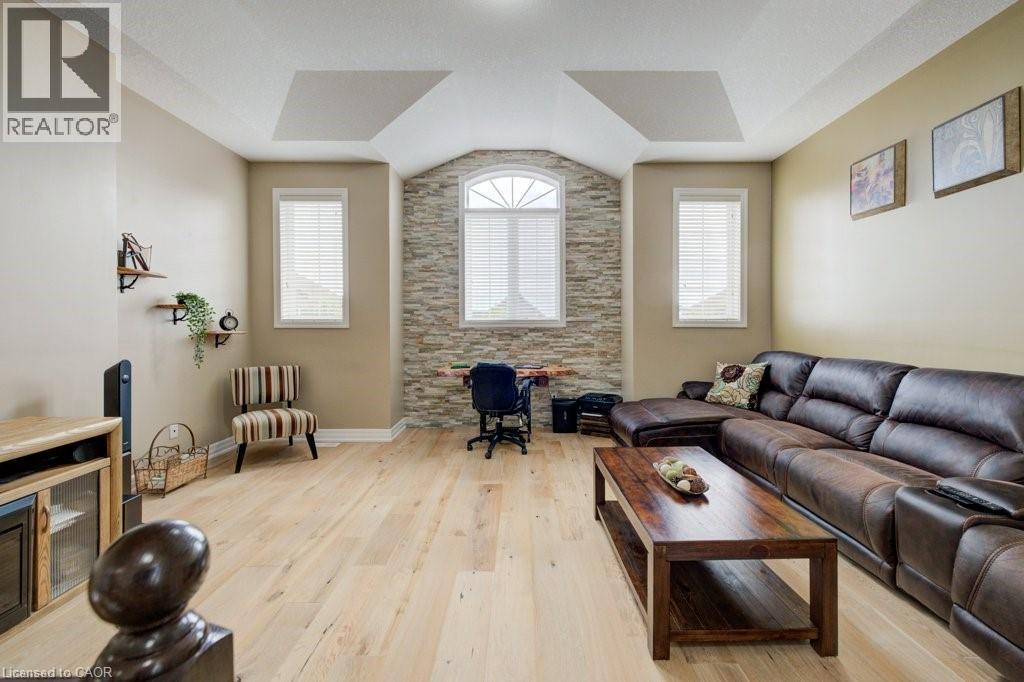 Living area featuring light wood-finish flooring, a tray ceiling, and a stone accent wall with an arched window - 300 Watervale Crescent, Kitchener, ON