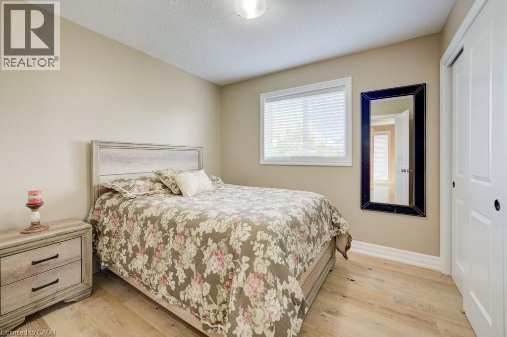 Bedroom featuring wood-finish flooring, neutral wall tones, a window with blinds, and white bi-fold closet doors - 300 Watervale Crescent, Kitchener, ON