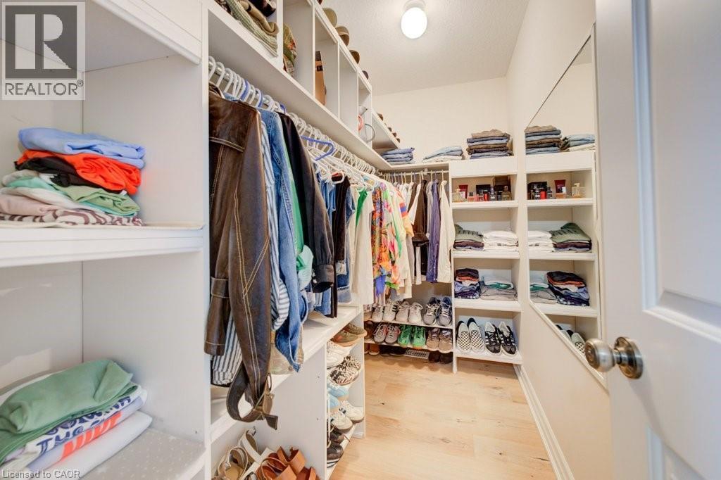 Walk-in closet featuring extensive built-in shelving, multiple hanging rods, dedicated shoe storage, a full-length mirror, and light wood-finish flooring - 300 Watervale Crescent, Kitchener, ON