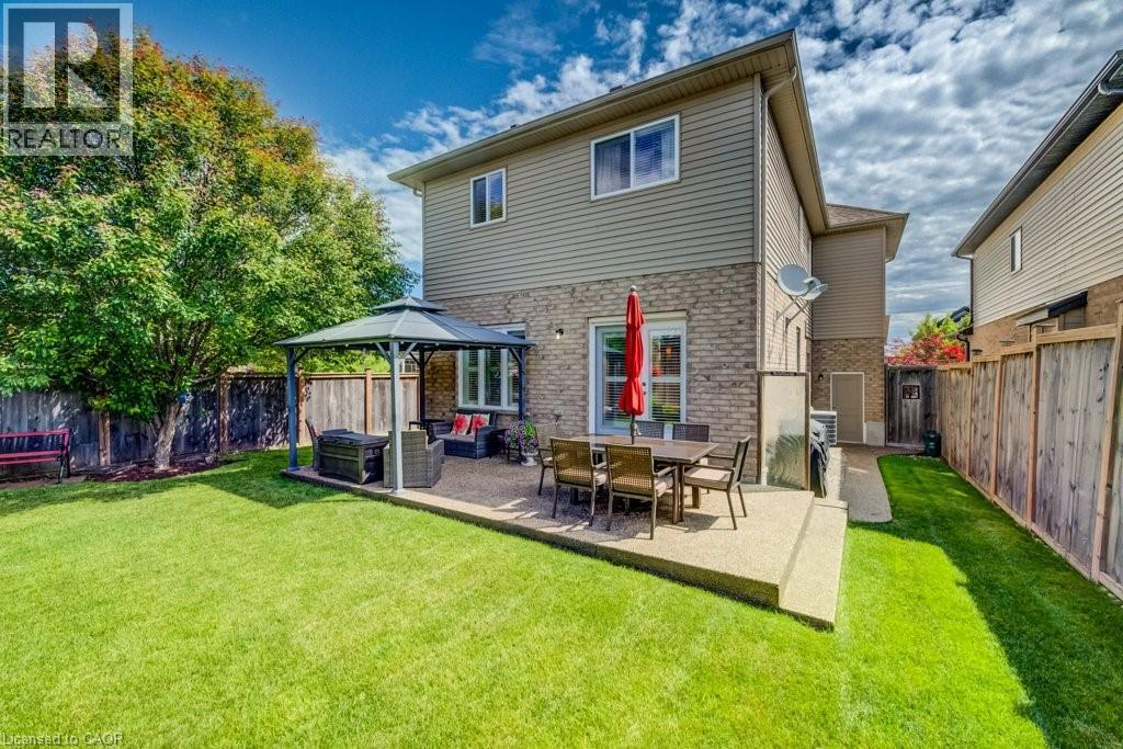 Rear exterior featuring a stone and siding facade, a concrete patio, a covered gazebo area, and a private fenced yard with mature trees - 300 Watervale Crescent, Kitchener, ON