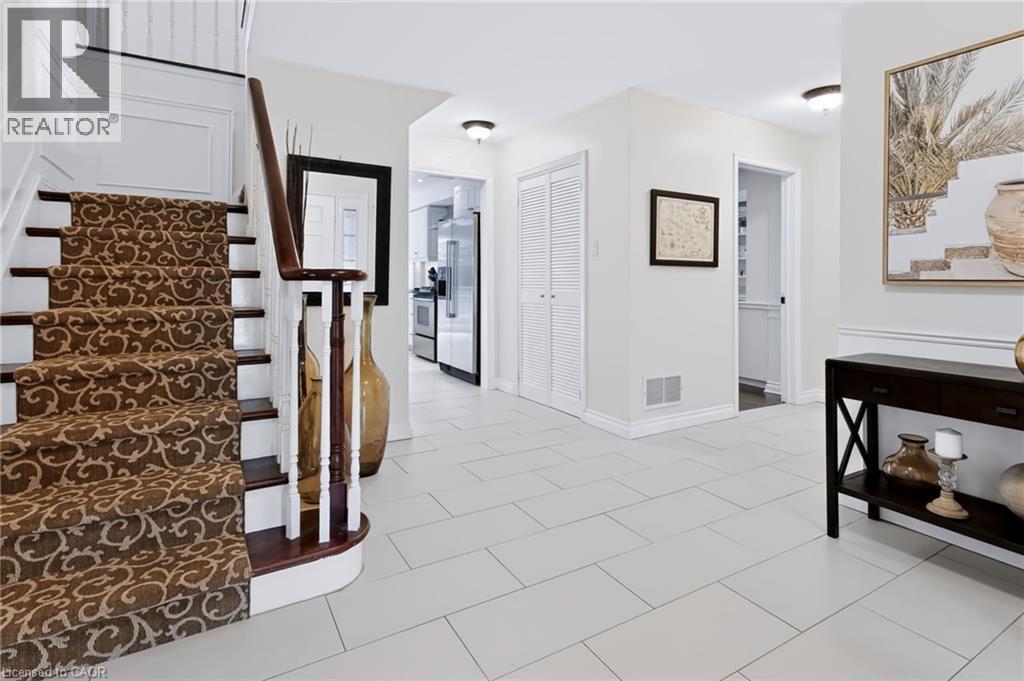 Gracious entryway featuring a curved staircase with a patterned runner, crisp white wainscoting, and large format tile flooring - 4248 Dunvegan Road, Burlington, ON