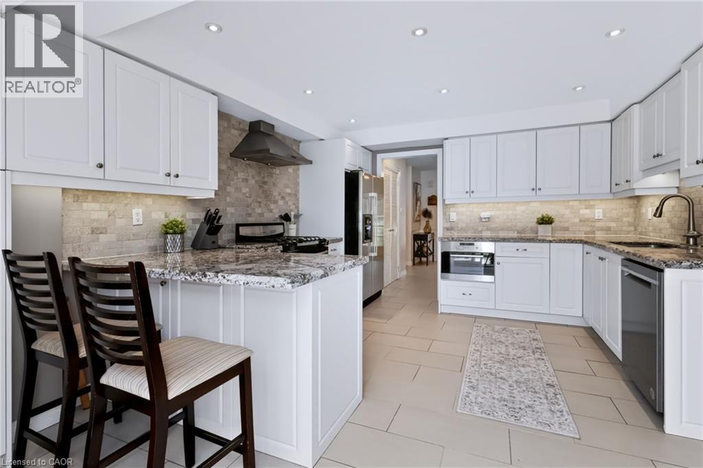 Contemporary kitchen featuring white cabinetry, stone countertops, a tile backsplash, stainless steel appliances, and recessed lighting - 4248 Dunvegan Road, Burlington, ON