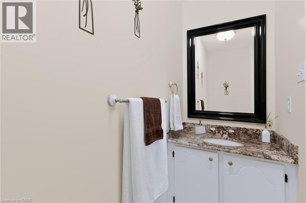 White vanity with arched panel doors, stone-finish countertop, undermount sink, and a framed mirror - 4248 Dunvegan Road, Burlington, ON