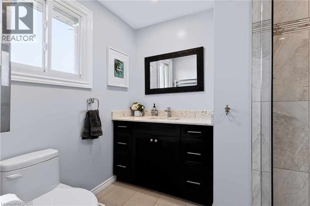 Single-handle chrome faucet, dark wood vanity with undermount sink, light-colored countertop, tiled flooring, and a large window - 4248 Dunvegan Road, Burlington, ON