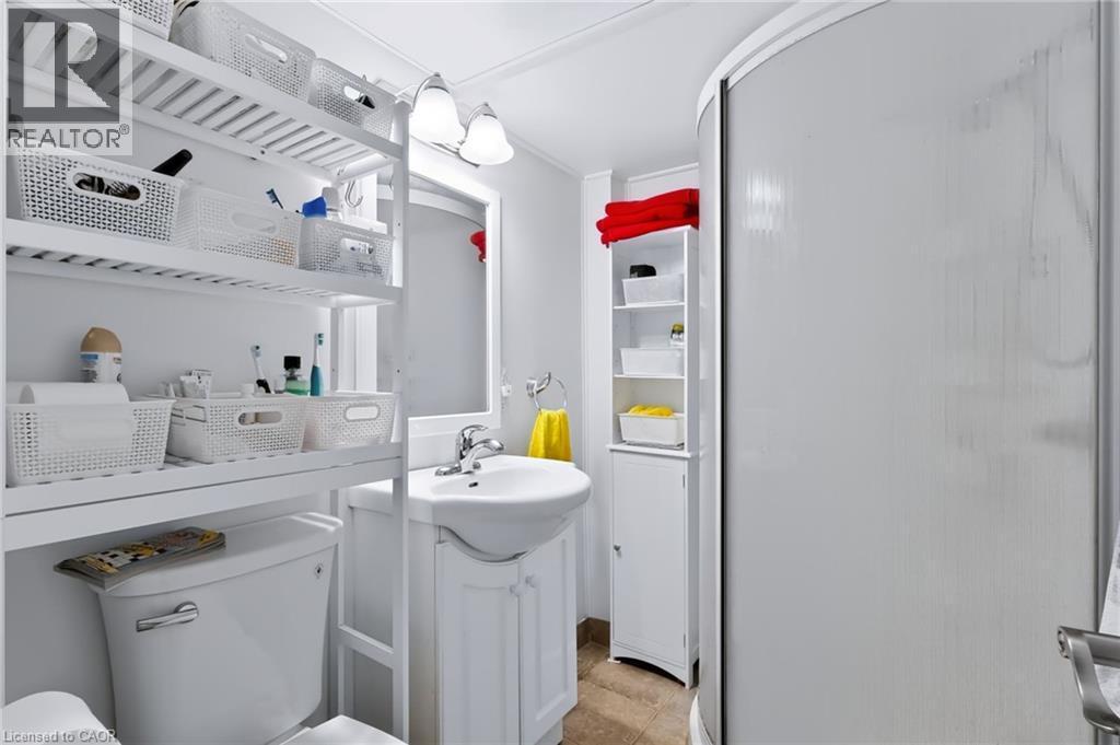 Curved shower enclosure, wall-mounted sink with cabinet, mirrored vanity, overhead lighting, and built-in shelving - 4248 Dunvegan Road, Burlington, ON