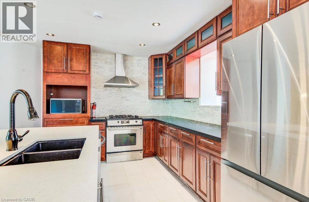 Kitchen featuring warm wood cabinetry, stainless steel appliances, a large island, and a dark undermount sink - 109 White Oak Place, Waterloo, ON - Indoor Photo Showing Kitchen With Double Sink