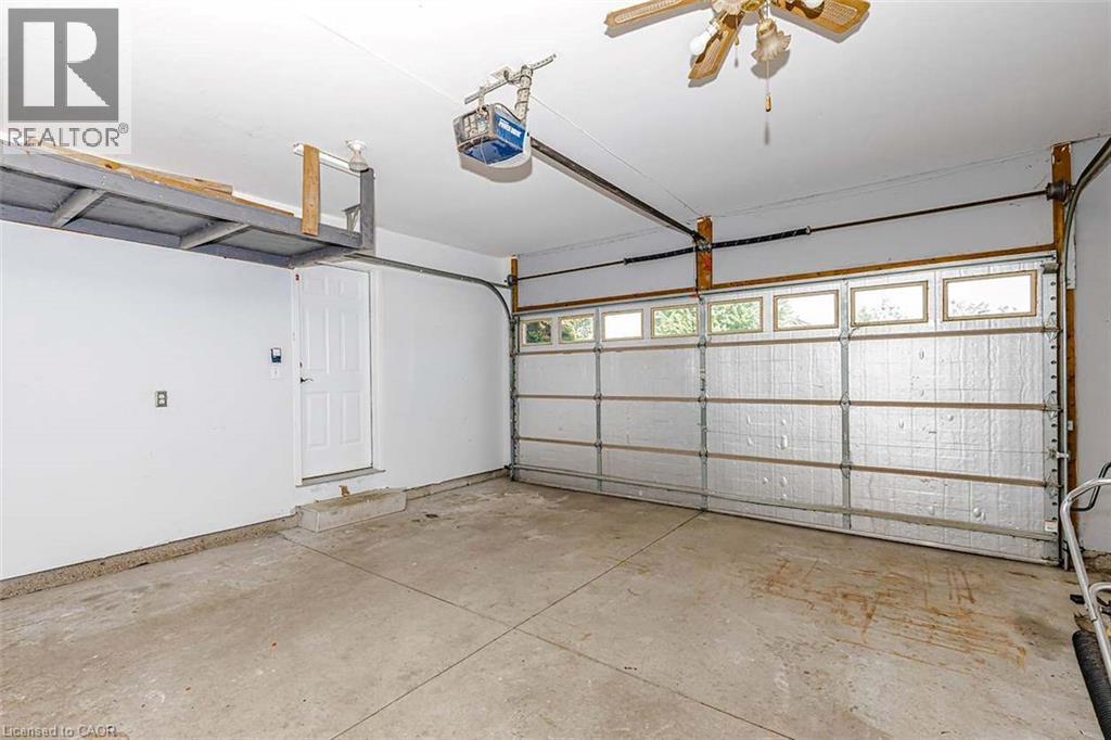 Attached garage with concrete flooring, overhead storage, side entry door, and garage door with upper window panels - 47 Queensway Drive, Strathroy, ON - Indoor Photo Showing Garage