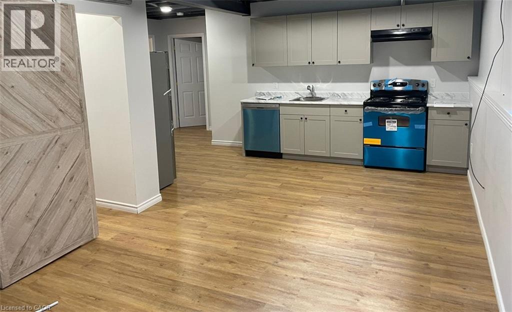 Wood-finish flooring, light grey cabinetry with black hardware, white countertops, and a white tile backsplash - 47 Queensway Drive, Strathroy, ON - Indoor Photo Showing Kitchen