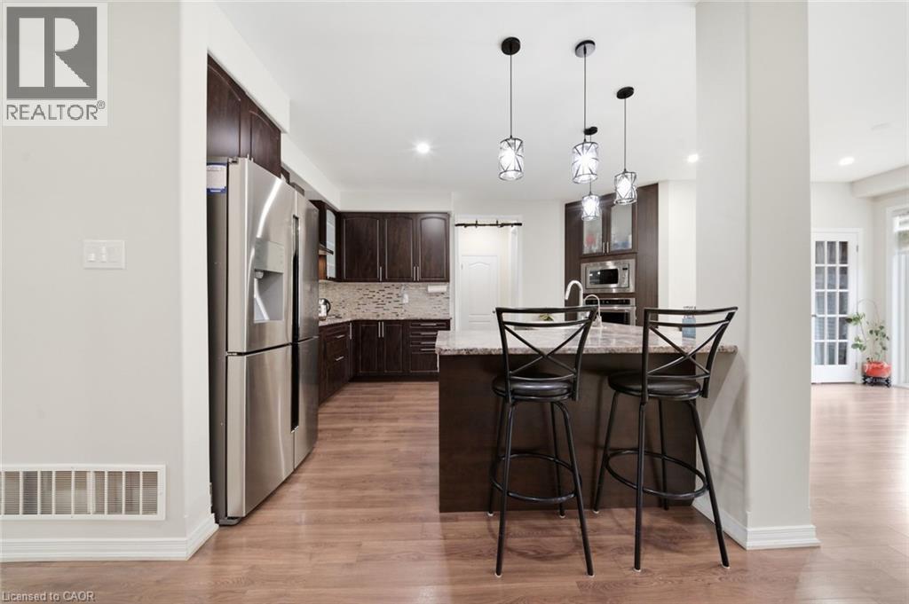 Kitchen featuring wood-finish flooring, dark wood cabinetry, stainless steel appliances, a tile backsplash, and a central island with pendant lighting - 57 Cheevers Road, Brantford, ON - Indoor Photo Showing Kitchen With Upgraded Kitchen