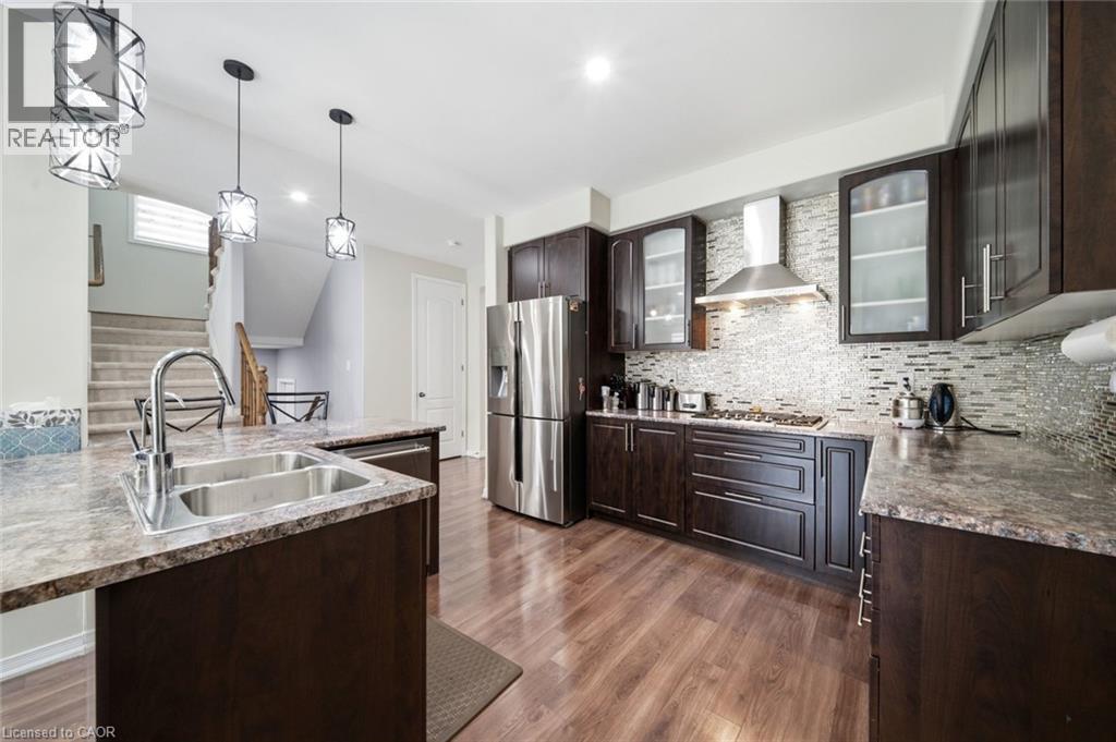 Kitchen featuring wood-finish flooring, dark wood cabinetry, a mosaic tile backsplash, stainless steel appliances, and a double basin sink with a gooseneck faucet - 57 Cheevers Road, Brantford, ON - Indoor Photo Showing Kitchen With Double Sink With Upgraded Kitchen