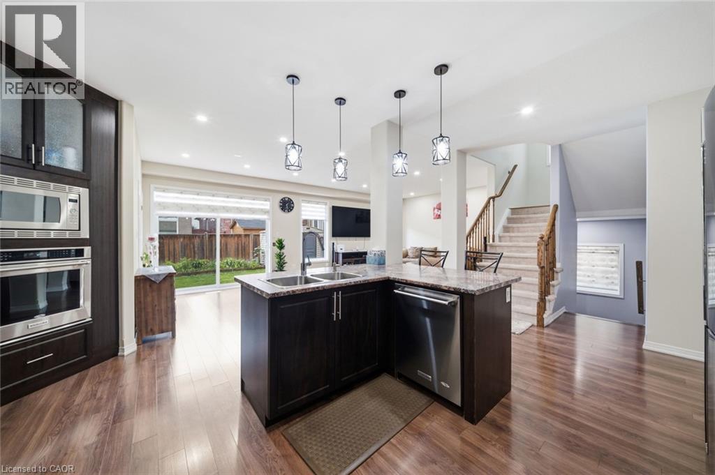 Kitchen featuring dark wood cabinetry, stainless steel appliances, a corner island with a double sink, and pendant lighting - 57 Cheevers Road, Brantford, ON - Indoor Photo Showing Kitchen With Double Sink With Upgraded Kitchen