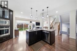 Kitchen featuring dark wood cabinetry, stainless steel appliances, a corner island with a double sink, and pendant lighting - 