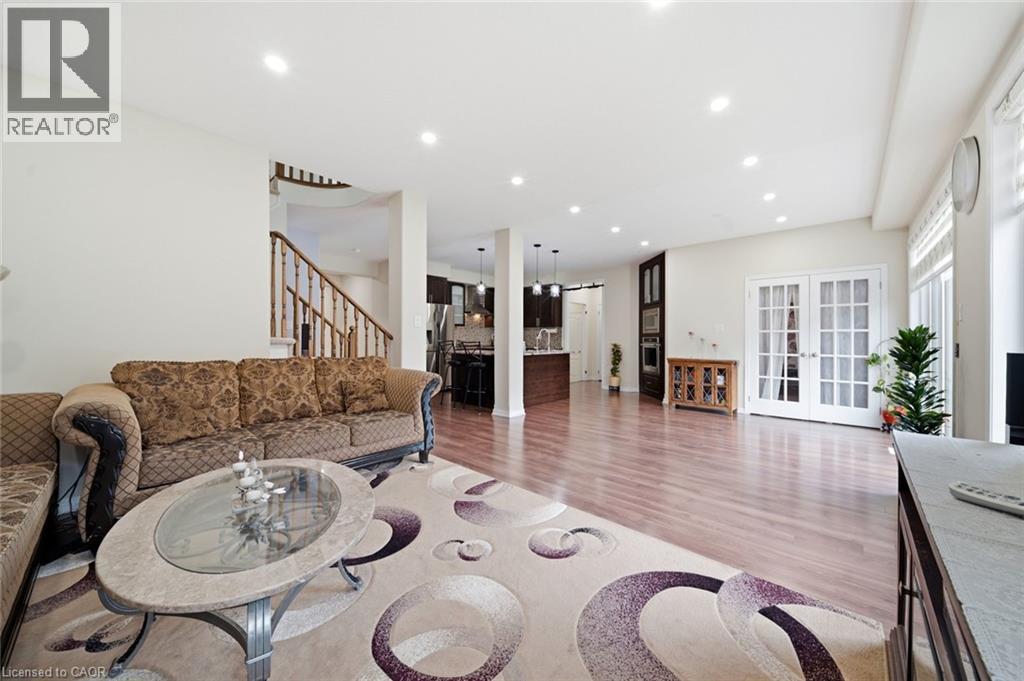 Recessed lighting, wood-finish flooring, staircase with wood railing, white French patio doors, and kitchen with dark cabinetry - 57 Cheevers Road, Brantford, ON - Indoor Photo Showing Living Room