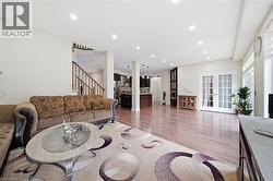 Recessed lighting, wood-finish flooring, staircase with wood railing, white French patio doors, and kitchen with dark cabinetry - 