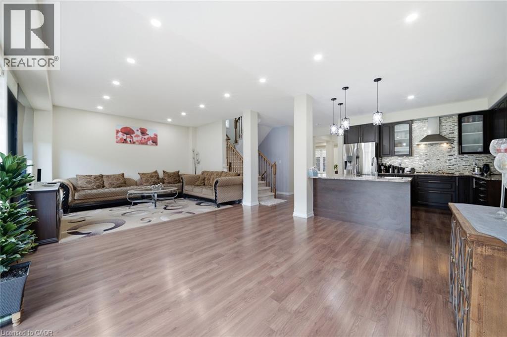 Recessed lighting throughout, wood-finish flooring, kitchen island with pendant lighting, stainless steel appliances, and a tiled kitchen backsplash - 57 Cheevers Road, Brantford, ON - Indoor Photo Showing Other Room