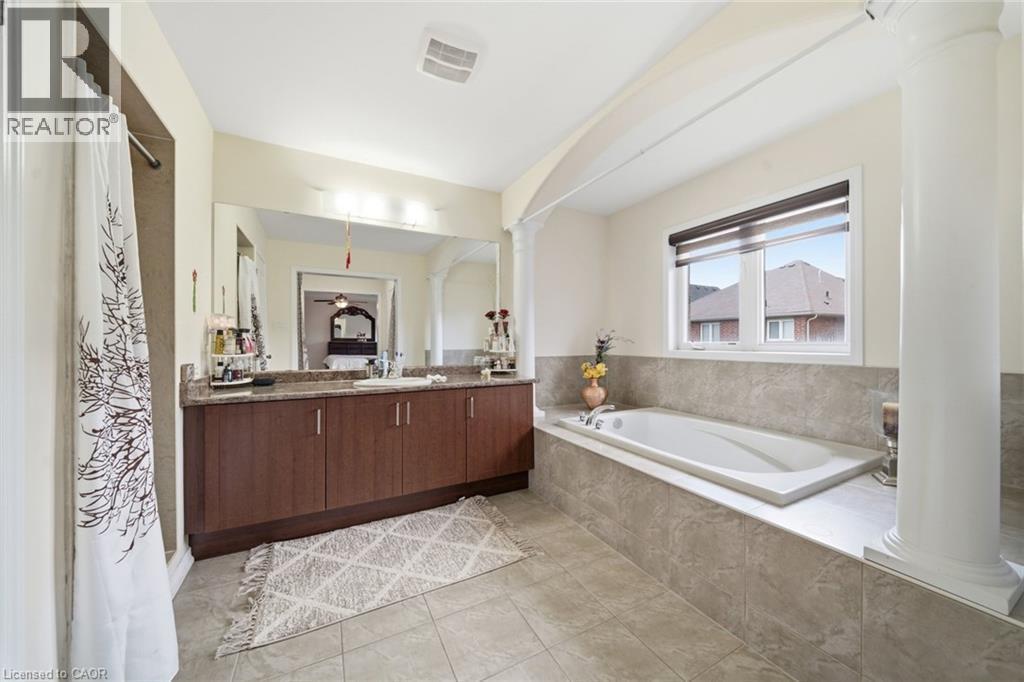 Built-in soaking tub with tiled surround, double vanity with stone-finish countertop, and integrated mirror - 57 Cheevers Road, Brantford, ON - Indoor Photo Showing Bathroom