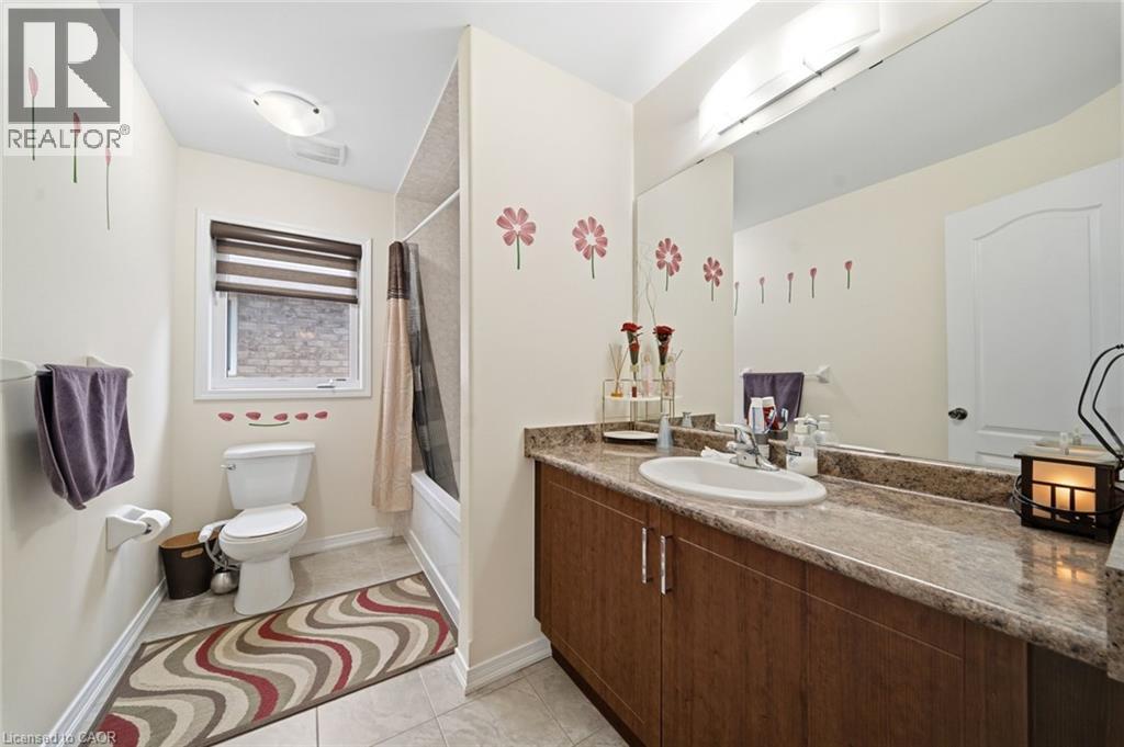 Vanity with integrated sink, full-width mirror, wood-finish cabinetry, and stone-finish countertop - 57 Cheevers Road, Brantford, ON - Indoor Photo Showing Bathroom
