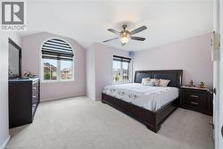 Arched window with integrated blinds, vaulted ceiling, ceiling fan with illumination, and plush carpet flooring - 