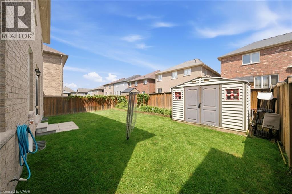 Expansive backyard featuring a green lawn, wood fence, and a storage shed with double doors - 57 Cheevers Road, Brantford, ON - Outdoor