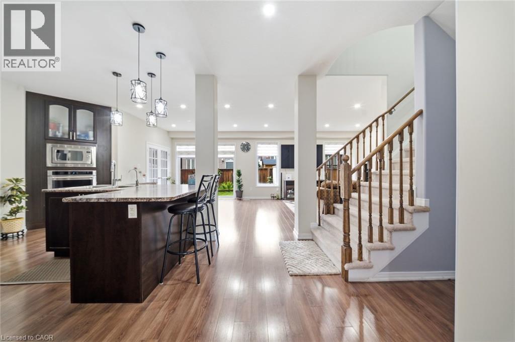 Open concept living space featuring wood-finish flooring, a kitchen island with stone countertop, built-in stainless steel appliances, pendant lighting, and a carpeted staircase with wood banister - 57 Cheevers Road, Brantford, ON - Indoor Photo Showing Kitchen With Upgraded Kitchen
