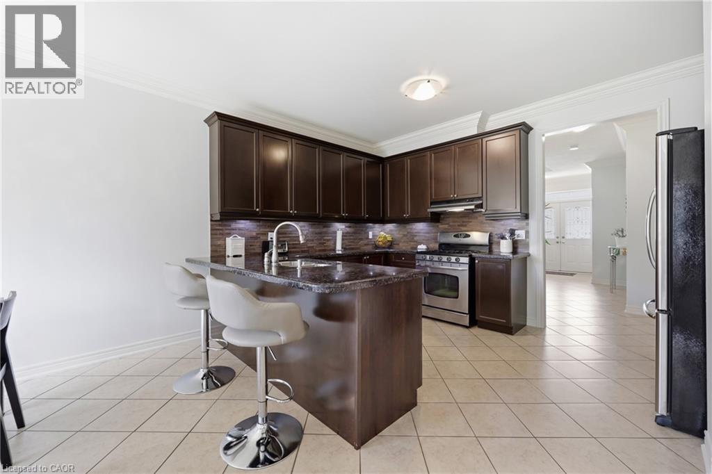 Dark wood-finish cabinetry, stainless steel appliances, a center island with sink, tile flooring, and crown molding - 738 Fourth Line, Milton, ON - Indoor Photo Showing Kitchen