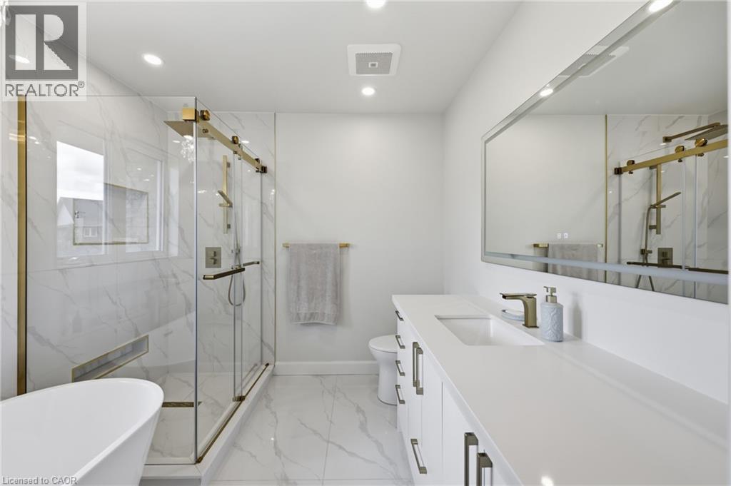 Spa-inspired primary bathroom featuring marble-look tile flooring, a freestanding soaking tub, and a spacious walk-in shower with frameless glass enclosure and brass hardware - 738 Fourth Line, Milton, ON - Indoor Photo Showing Bathroom